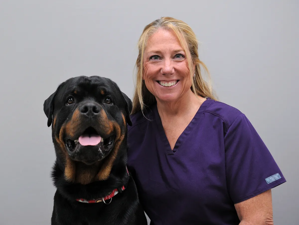 Smiling veterinarian in purple scrubs poses with a black and tan Rottweiler wearing a red collar, representing compassionate pet care at an independent animal hospital in Centerville, Ohio